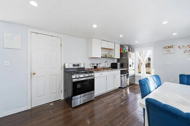 a kitchen with stainless steel appliances a stove a sink a refrigerator white cabinets and wooden floor