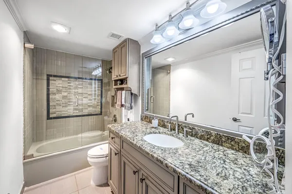 a bathroom with a granite countertop sink vanity mirror bathtub shower and a toilet