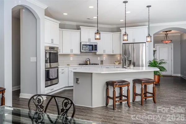a kitchen with stainless steel appliances granite countertop a dining table chairs refrigerator and sink