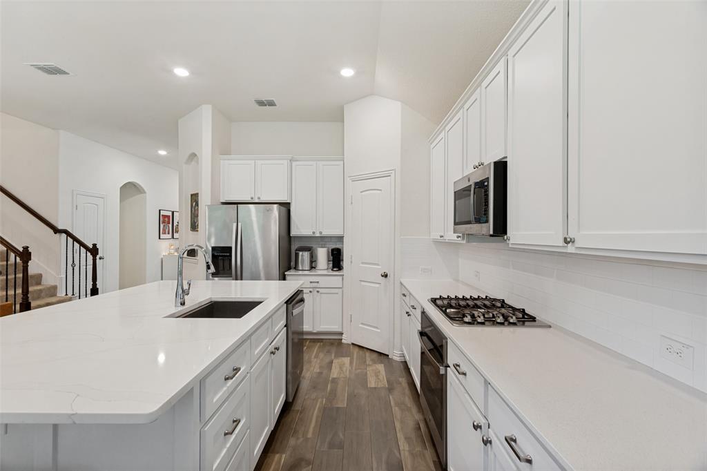 5556 Vaquero Road Fort Worth, TX 76126 - Photo 12 of 25 Kitchen featuring a large central island with an undermount sink, white cabinetry, integrated stainless steel appliances (gas cooktop), and wood-finish flooring