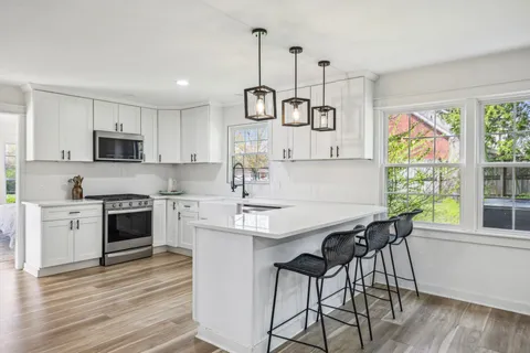 a kitchen with stainless steel appliances granite countertop a stove a sink a microwave a refrigerator and white cabinets with wooden floor