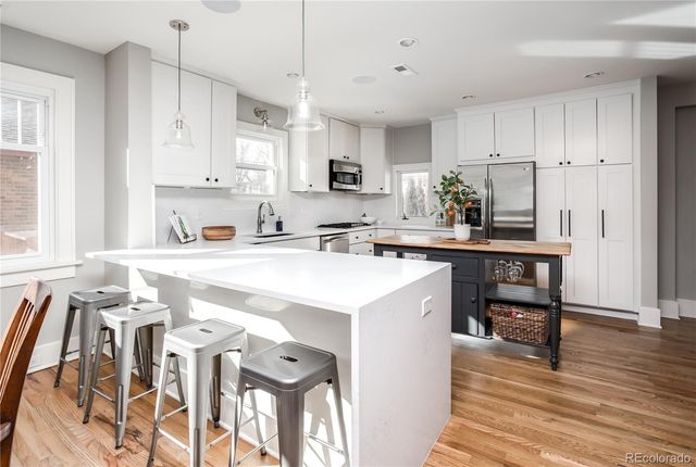 a kitchen with stainless steel appliances a sink a stove a refrigerator cabinets and dining table with wooden floor