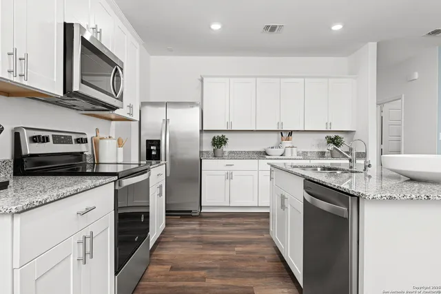 a kitchen with stainless steel appliances granite countertop a stove top oven a sink dishwasher and a refrigerator with wooden cabinets