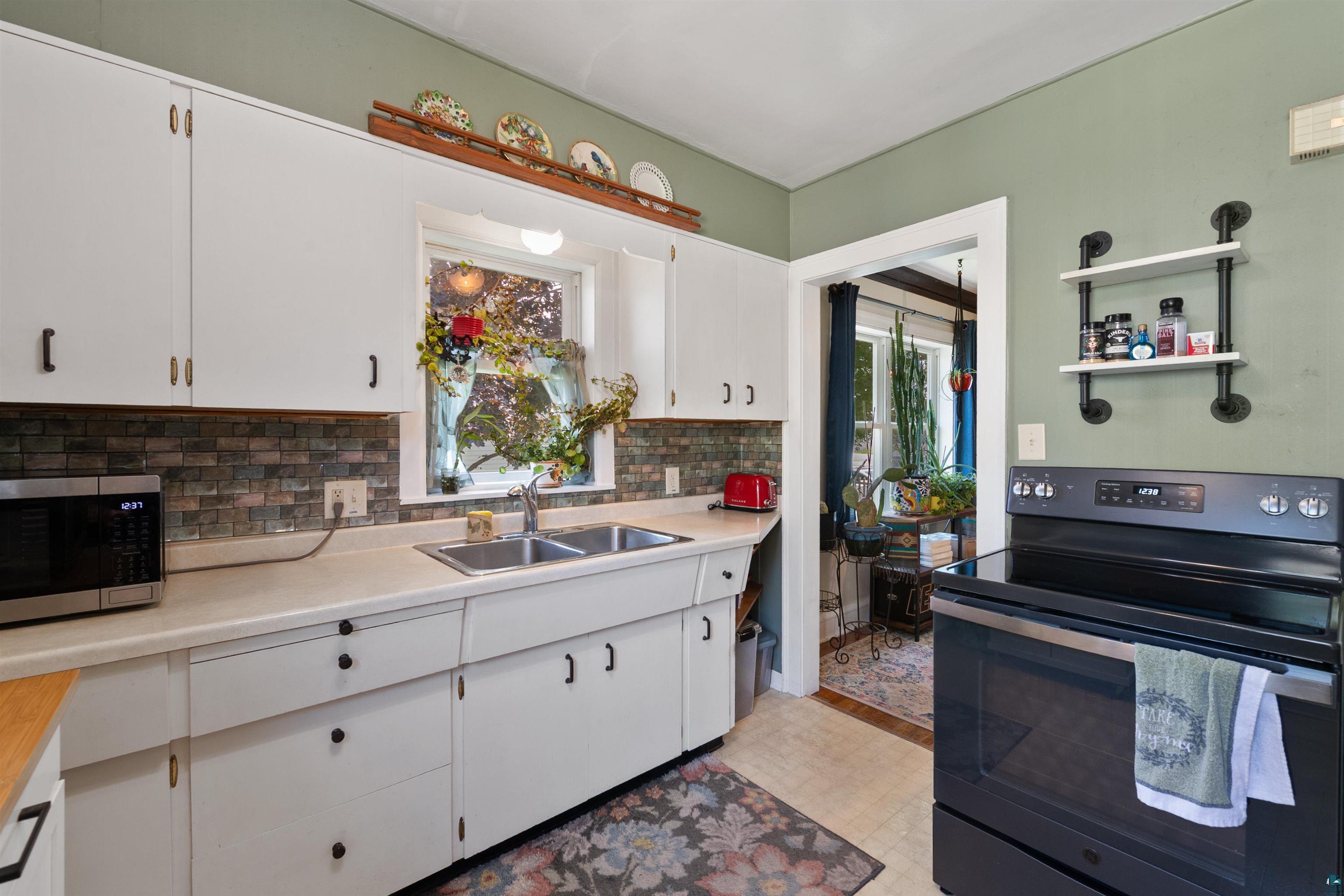 3209 Chestnut Street Duluth, MN 55806 - Photo 16 of 28 Kitchen featuring white cabinetry, a double basin sink, and a dark tile backsplash