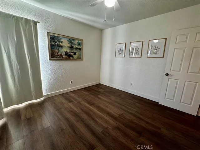 a view of an empty room with wooden floor and a ceiling fan