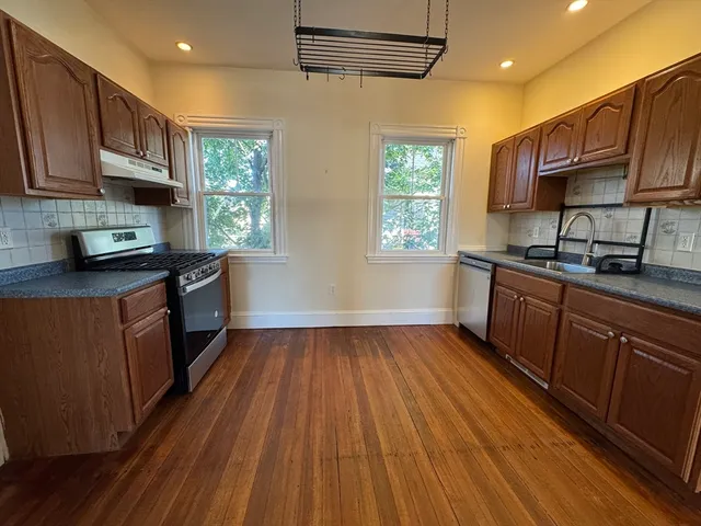 a kitchen with stainless steel appliances granite countertop wooden cabinets a stove a sink and dishwasher with wooden floor