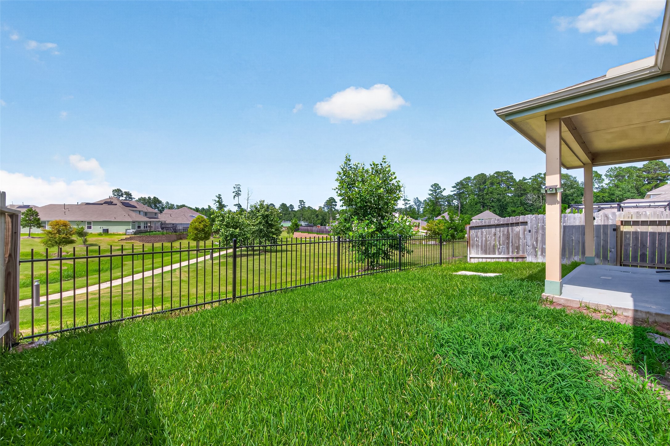 2526 Sturgeon Way Conroe, TX 77384 - Photo 41 of 49 Spacious backyard with a well-maintained lawn, covered patio, and a scenic view of a grassy area and trees beyond a black metal fence. Ideal for outdoor relaxation and entertaining.