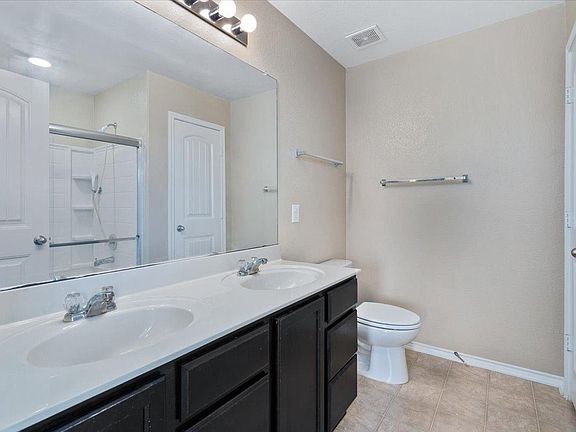 904 Lonesome Lilly Way Pflugerville, TX 78660 - Photo 27 of 34 Bathroom featuring a double vanity with two undermount sinks, a shower with a sliding glass door, and a toilet