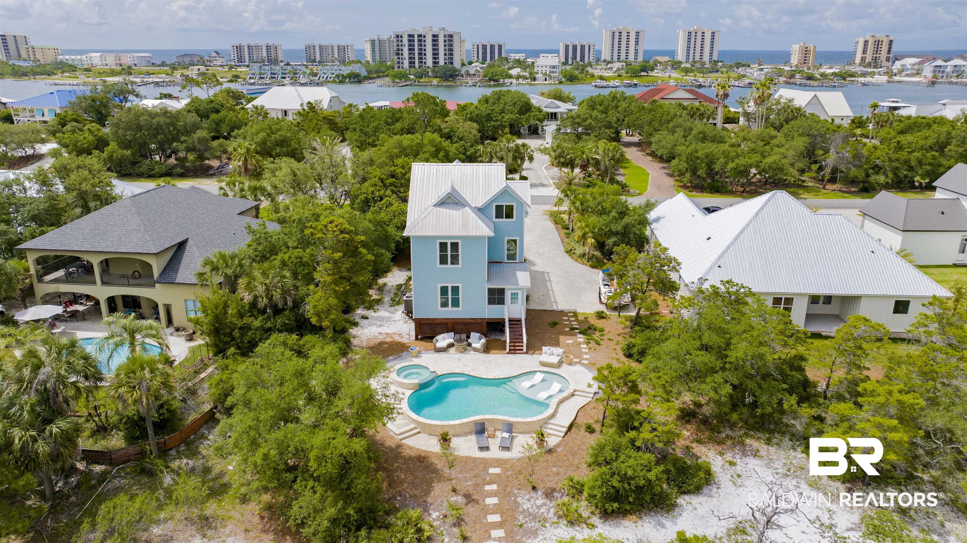 30351 River Road Orange Beach, AL 36561 - Photo 42 of 44 Light blue multi-story residence with a metal roof and an elevated foundation, featuring a private swimming pool with an integrated spa