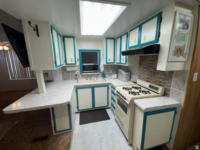 1225 North Dixie Downs Road, Unit 100 St. George, UT 84770 - Photo 10 of 22 U-shaped kitchen featuring white cabinetry with teal accents, a gas range, a multi-toned tile backsplash, and a white countertop