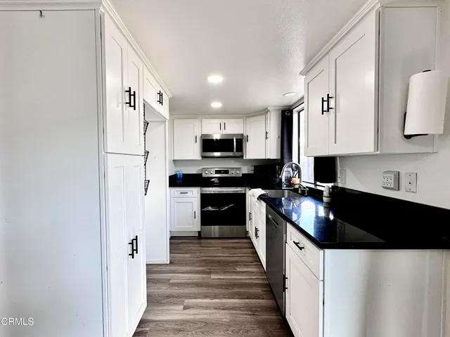 a kitchen with granite countertop a refrigerator a sink and white cabinets