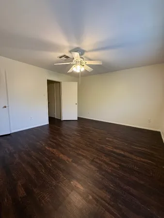 a view of an empty room with wooden floor and a ceiling fan