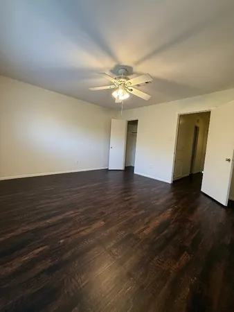 a view of an empty room with wooden floor and a ceiling fan
