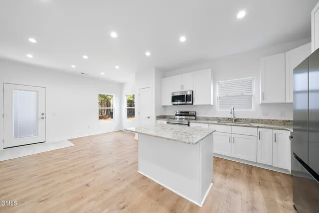 a large kitchen with stainless steel appliances granite countertop a stove a sink and white cabinets with wooden floor