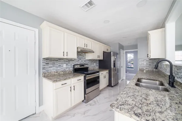 a kitchen with granite countertop a sink stainless steel appliances and white cabinets