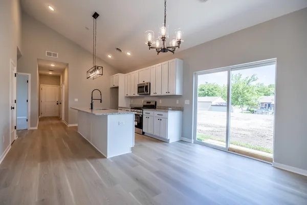 a large kitchen with kitchen island a large counter space a sink appliances and a chandelier