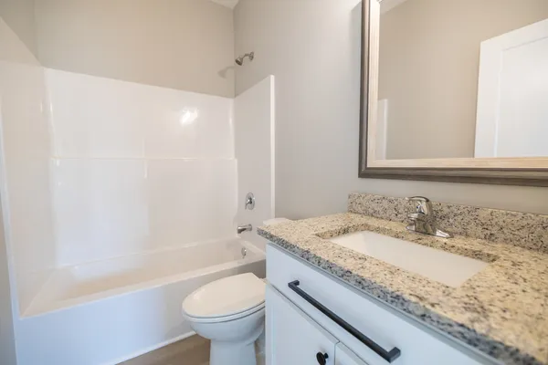 a bathroom with a granite countertop sink a toilet a mirror and bathtub