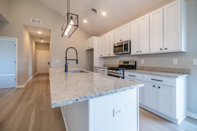 a kitchen with stainless steel appliances granite countertop a sink a stove and a wooden floors