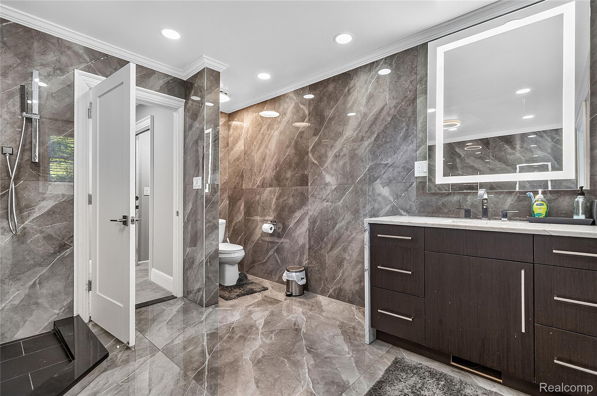 15879 Millar Road Clinton Township, MI 48036 - Photo 23 of 65 Full wall and floor tile in a marble-look finish, dark wood-finish vanity with ample storage, integrated dual sinks, and an illuminated mirrored cabinet