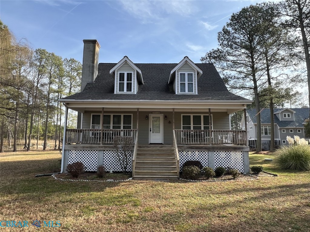 View of front of property with covered porch, roof with shingles, a front yard, and a chimney