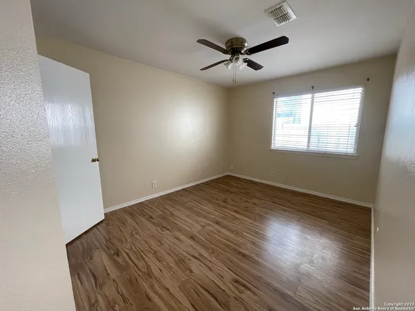 an empty room with wooden floor fan and windows