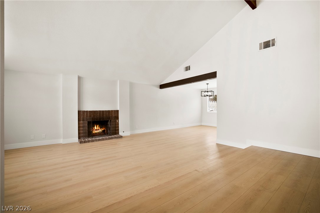 2411 Doherty Way Henderson, NV 89014 - Photo 4 of 34 A spacious living room features a brick fireplace and gleaming hardwood floors, creating a warm, inviting atmosphere.