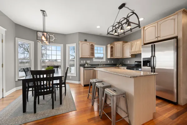 a kitchen with stainless steel appliances granite countertop a dining table chairs refrigerator and microwave