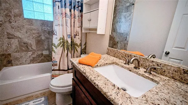 a bathroom with a granite countertop bathtub sink vanity mirror and toilet