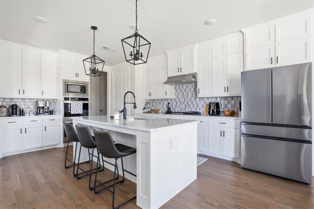 4202 Crown Run Road Midlothian, TX 76065 - Photo 10 of 34 Kitchen featuring an expansive island with seating, white shaker cabinetry, stainless steel appliances, wood-finish flooring, and pendant lighting
