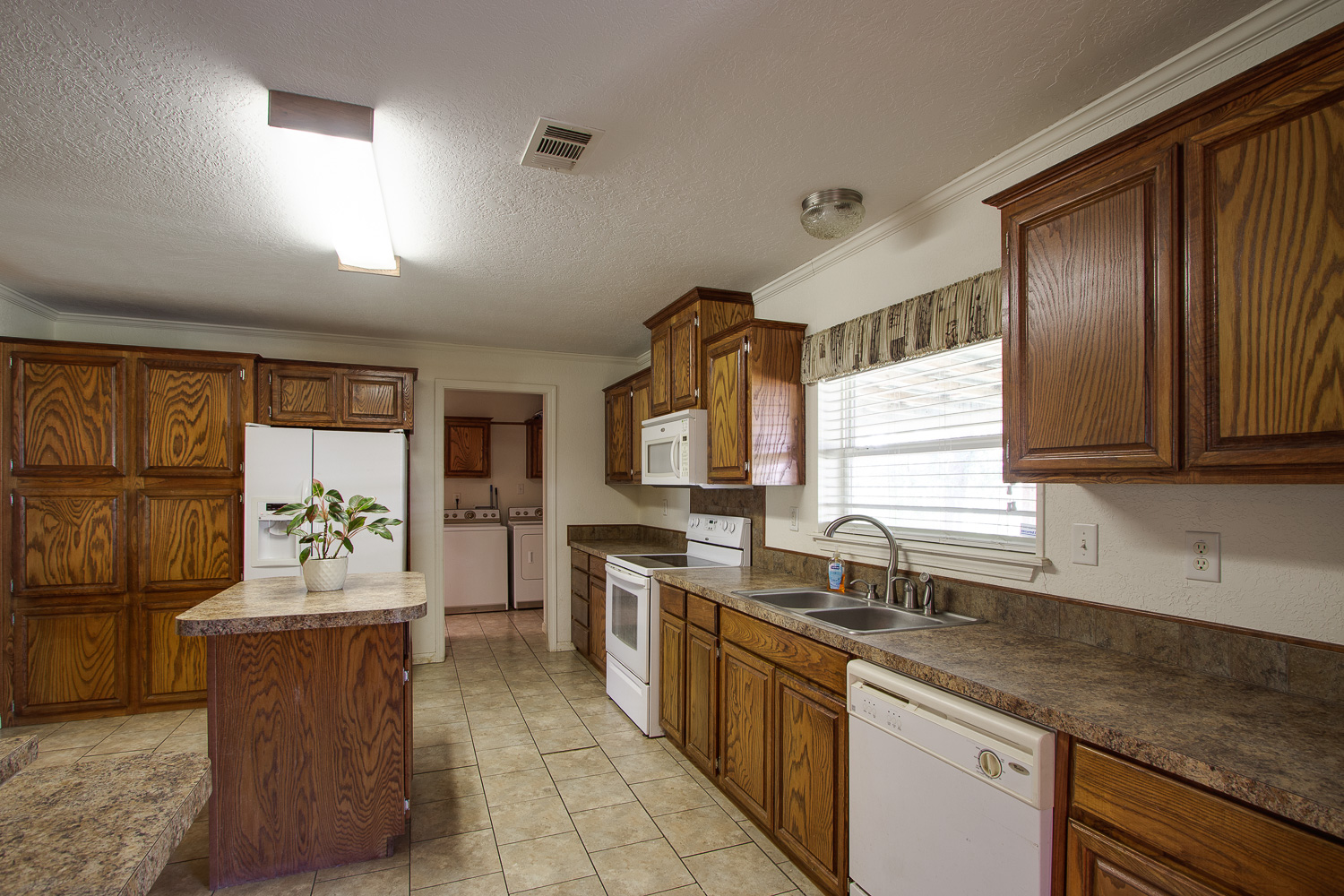 133 Mark Adams Road Del Valle, TX 78617 - Photo 7 of 20 Oak cabinetry paired with durable tile flooring anchors this fully equipped kitchen workspace.