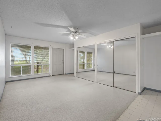 an empty room with chandelier fan and windows