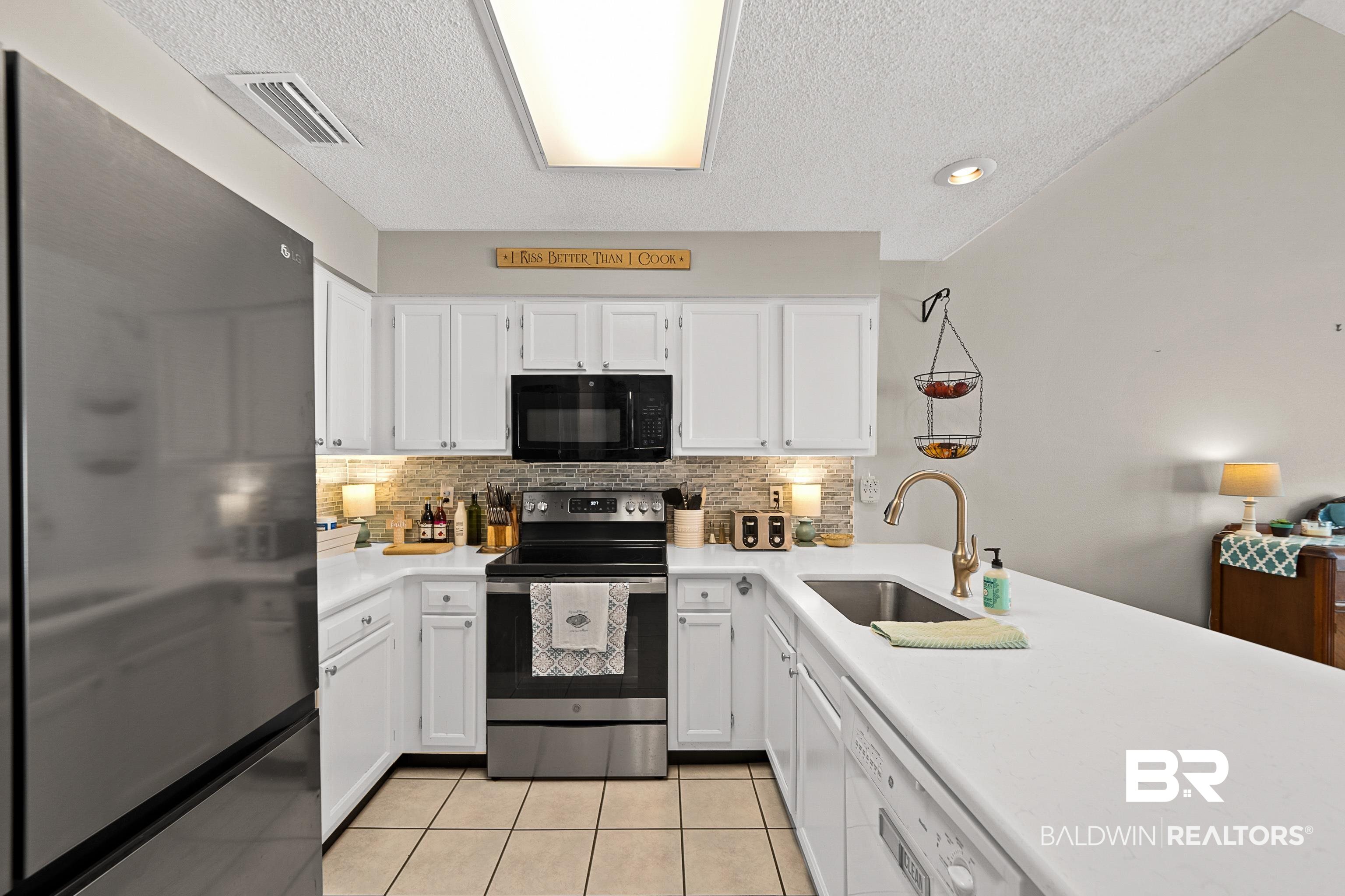 1701 Regency Road, Unit 106 Gulf Shores, AL 36542 - Photo 7 of 42 Kitchen with appliances with stainless steel finishes, white cabinetry, light tile patterned floors, decorative backsplash, and a textured ceiling