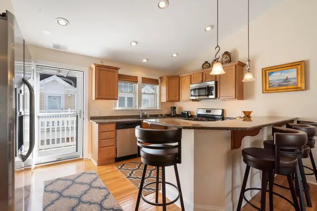 a kitchen with stainless steel appliances granite countertop a stove top oven a sink a dining table and chairs with wooden floor