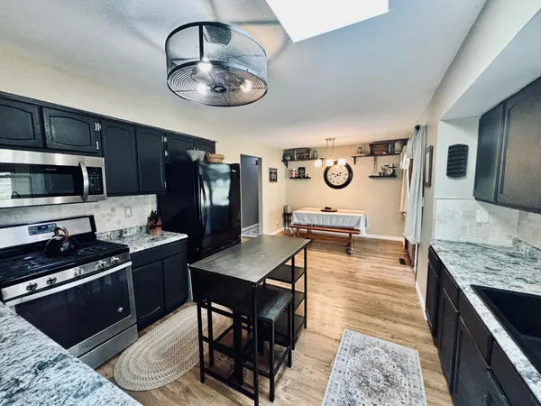 a kitchen with stainless steel appliances granite countertop a stove top oven a sink a dining table and chairs