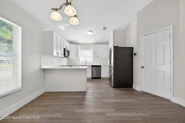 a kitchen with stainless steel appliances granite countertop a refrigerator a sink dishwasher a stove and white cabinets with wooden floor