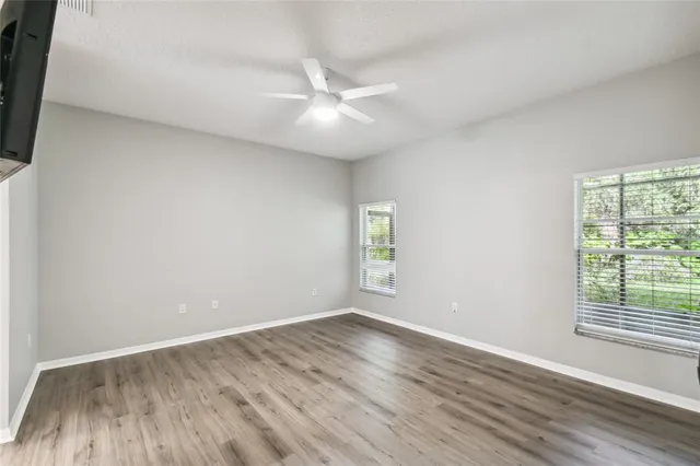 an empty room with wooden floor fan and windows