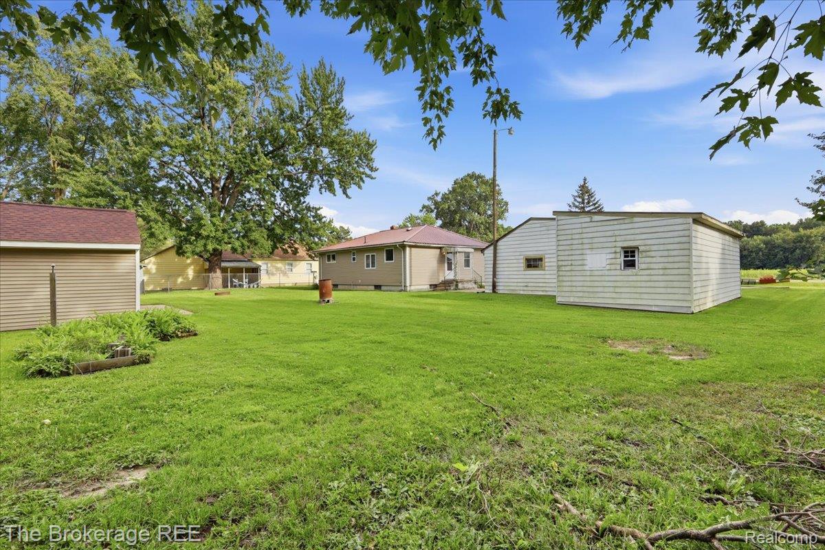11973 East Brooks Road Lennon, MI 48449 - Photo 28 of 28 Expansive green lawn with established trees, featuring a detached shed with horizontal siding and a reddish roof, a screened-in structure with a gabled roof, and a second detached structure with horizontal siding and multiple windows