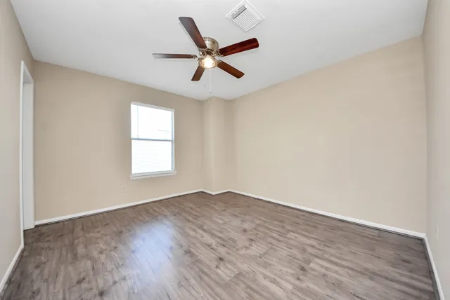 an empty room with wooden floor fan and windows