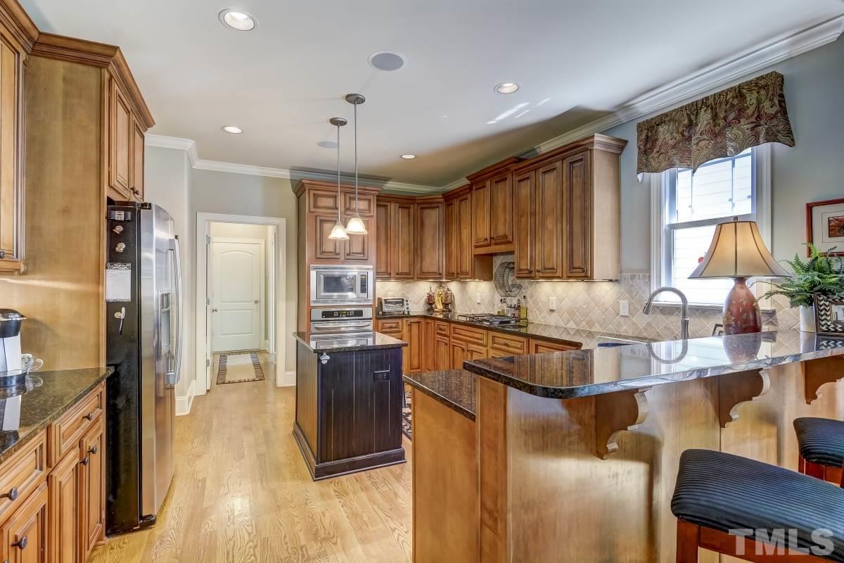 7207 Newport Avenue Raleigh, NC 27613 - Photo 10 of 25 a kitchen with stainless steel appliances granite countertop a refrigerator a sink a stove and white cabinets with wooden floor