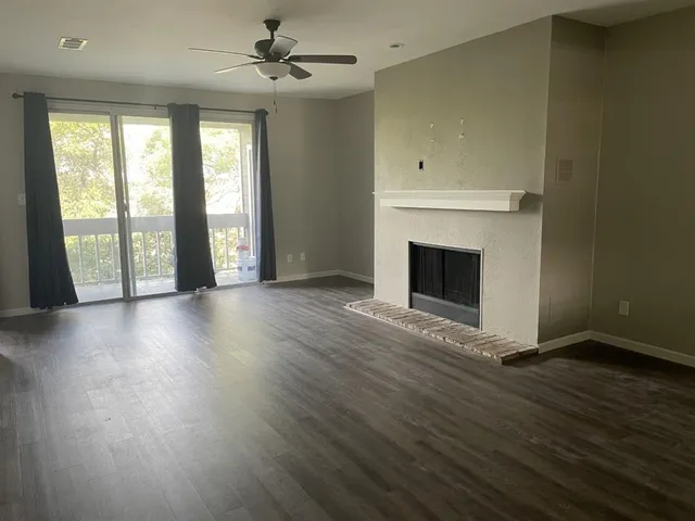 an empty room with wooden floor fireplace and windows