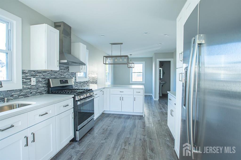 a large kitchen with a stove a sink dishwasher a refrigerator and white cabinets with wooden floor