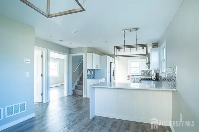 a kitchen with stainless steel appliances granite countertop a refrigerator a sink dishwasher a stove and white cabinets with wooden floor