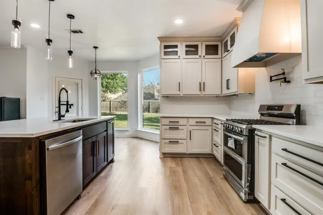 a kitchen with stainless steel appliances white cabinets a sink dishwasher a stove and a refrigerator with wooden floor