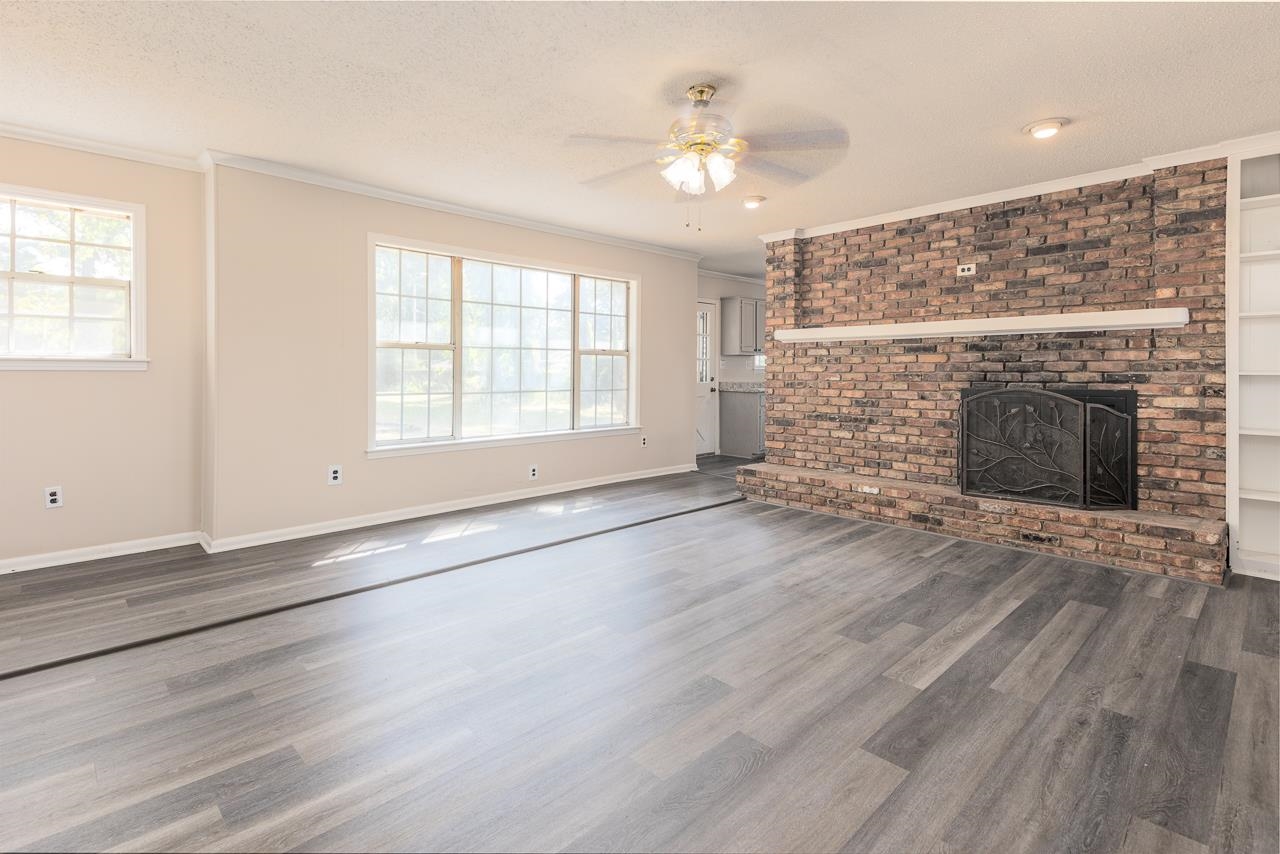 2718 Kate Bond Road Memphis, TN 38133 - Photo 4 of 39 Unfurnished living room featuring ornamental molding, ceiling fan, a brick fireplace, dark wood finished floors, and a textured ceiling