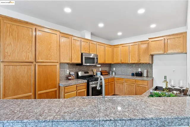 a kitchen with stainless steel appliances granite countertop a stove top oven a sink a refrigerator and cabinets