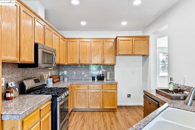 a kitchen with stainless steel appliances granite countertop wooden cabinets a stove top oven a sink and dishwasher with wooden floor