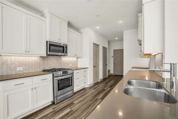 a kitchen with stainless steel appliances a stove a sink a refrigerator and white cabinets with wooden floor