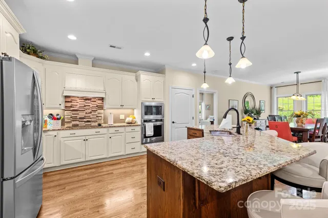 a kitchen with stainless steel appliances granite countertop a kitchen island a stove a refrigerator a oven a sink with island chairs and couches
