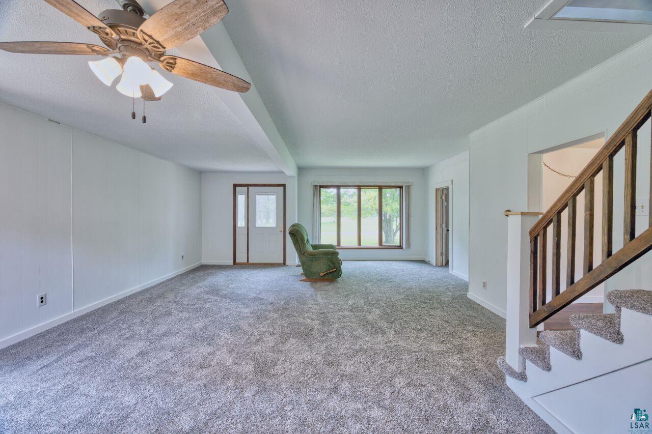 4755 Judd Road Gilbert, MN 55741 - Photo 6 of 50 Unfurnished living room featuring a textured ceiling, carpet, stairs, baseboards, and ceiling fan