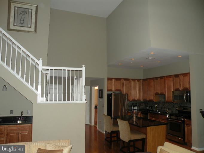 12000 Market Street, Unit 438 Reston, VA 20190 - Photo 7 of 13 a kitchen with stainless steel appliances kitchen island granite countertop a refrigerator a stove a sink a dining table and chairs with wooden floor